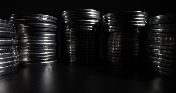 Curly lines of stacks made of silver coins standing on black table in dark premise with poor light. Money investments and accumulation concept