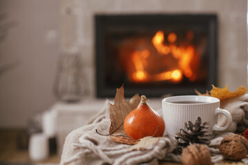 Cozy autumn. Warm cup of tea, pumpkins, autumn leaves, cones, cozy scarf on rustic wooden table on...