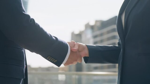 Close-up gimbal shot two business partners male female handshaking meet and shake hands standing outdoors on office building rooftop terrace overlooking high-rise skyscrapers modern city downtown