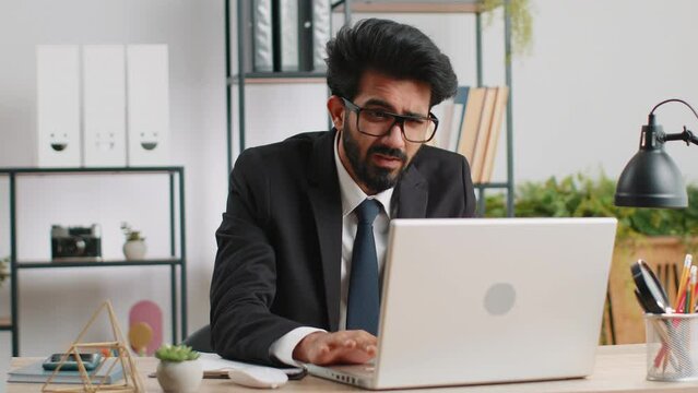 Irritated tired indian business man while working on laptop, unexpected online website problem, computer virus data loss by hacking. Freelancer feeling mad about broken notebook at office workplace