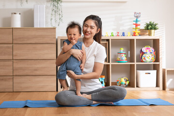 Asian mom playing to adorable infant baby on yoga mat smiling and happiness at home. Mom talking with baby fun and laughing throwing up son in the air exercise together. Relax time.Baby and Mother day