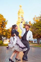 full body portrait young adult latin american couple dancing cueca traditional dance with huaso dress in the city square of La Serena	