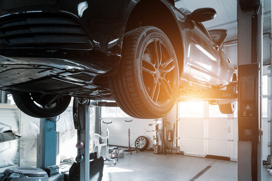Car service center. Bottom behind pov vehicle raised on lift technician worker perform diagnosticas and inspection at maintenance station . Automobile repair and check up at workshop garage