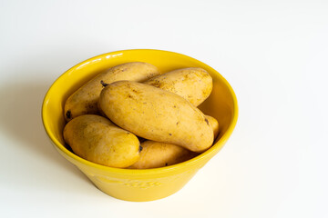 Closeup view of group of fresh ripe mango fruit in bright yellow ceramic bowl isolated on white background
