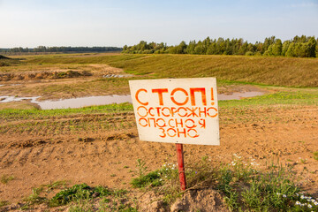 Sign with the words Stop. Caution, Dangerous Zone next to the developed sand quarry. Russia