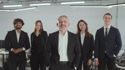 The director of a consulting firm stands with his employees. People in business suits pose against the backdrop of the office.