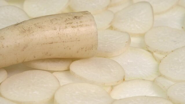 Sliced daikon radish and root rotates on a plate as a background. Mooli or Daikon, Raphanus sativus, displayed on a market stall, traditional japanese dish