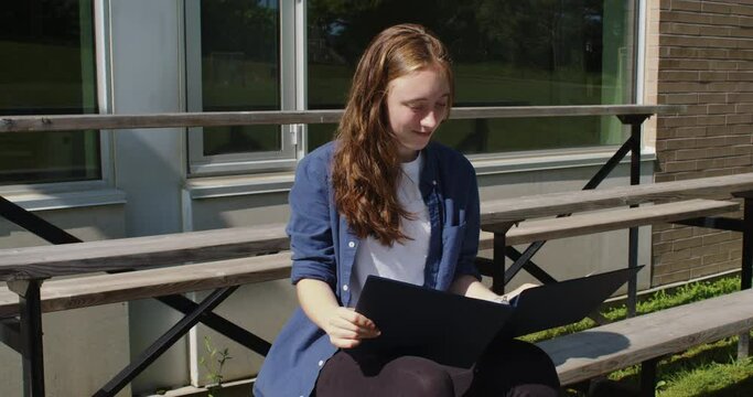 Happy student sitting on bleachers while studying in front of a school