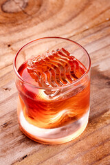 negroni drink with rippled professional rind ice on wooden table angle view portrait