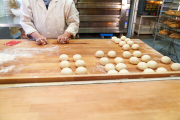 Skilled baker shaping raw burger bun molds by hand in a bakery, ready to bake them into perfect...