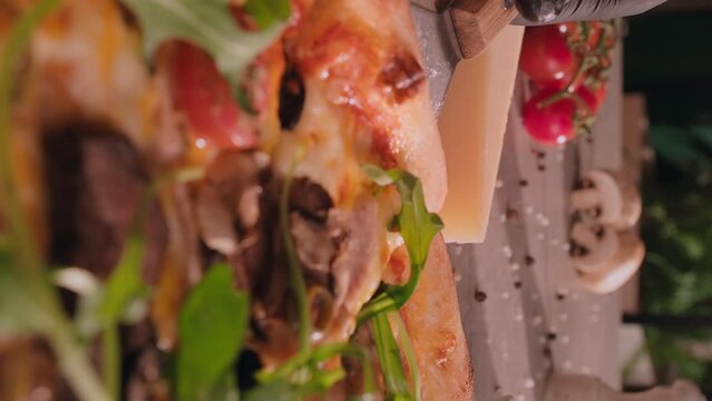 Closeup shot of a slice of cheesy meat pizza with aragula. Hand taking meat pizza slice via spatula. Fast-food menu concept