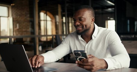 A man with a Black skin color works in the office at the same time on a laptop and on a phone