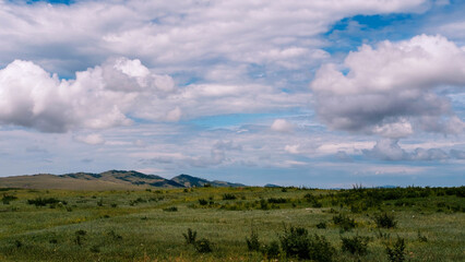 Photo of the steppe in summer, with beautiful clouds in the blue sky, the endless steppe at the foot of high hills under a warm summer sky. Khakassia, Siberia, Russia.