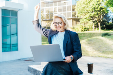 Excited happy middle aged business woman with laptop outdoors feeling winner rejoicing online win got new job opportunity, overjoyed motivated lady doing yes gesture, receive good results, celebrating