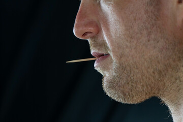 Man with a toothpick in his mouth close up profile face, background selective focus, copy space people theme, story tel8ng. - obrazy, fototapety, plakaty