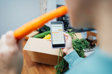 Woman holding phone with active online mobile app of Veganuary diet calendar and eating fresh...