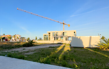 Villa under construction. Tower crane on construction site. Prefabricated home сonstruction at Mediterranean sea. Construction of modern house on coastline in Spain. Home renovation. Build new home.