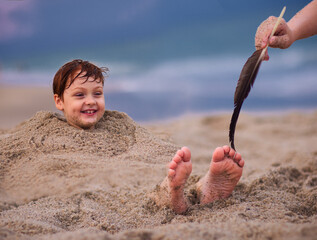 tickling kid's feet in a sand. family having fun on sandy beach. summer activity. coastal vacation