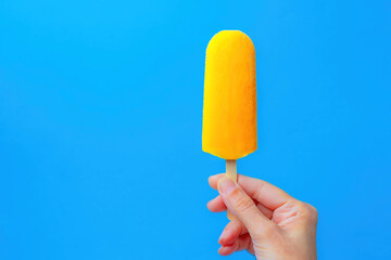 mango-flavored popsicle in a woman's hand on a blue background
