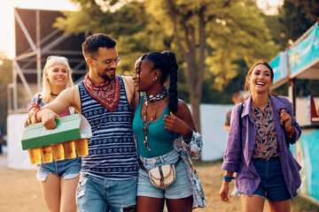 Cheerful friends carrying package of draft beer while attending summer music festival.