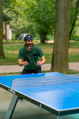 Inclusiveness An elderly focused man with long hair and a gray beard plays ping pong in a city park 
