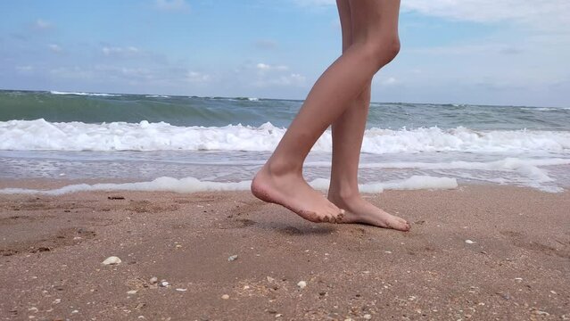 Close-up of bare male feet walking along the sandy coast on a summer day. Legs of a walking man on a sandy beach against the background of the sea, slow motion. 
