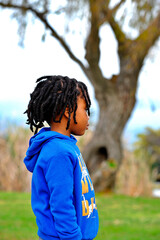 Fototapeta premium Portrait Photo of beautiful young black African boy with dreadlocks standing in a park.