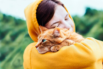 Beautiful pretty girl hugging a cute ginger cat on a blurred background. Close up portrait of a young hipster woman hugging her good friend ginger cat. Relaxation, pleasure. People and animals in love