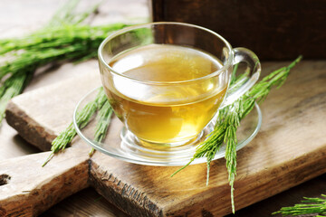 Horsetail tea or extract in glass cup with fresh leaf on wooden rustic background, closeup, natural treatment for hair and skin care, source of silica, detox and bone osteoporosis remedy