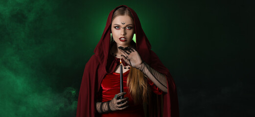 Beautiful witch with candle on dark green background