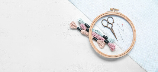 Wooden embroidery hoops with scissors, threads and canvas on light background with space for text
