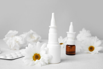 Fototapeta na wymiar Nasal drops with pills, flowers and tissues on table near grey wall. Seasonal allergy concept
