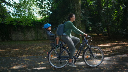 Mother riding bicycle outside at park with kid in back seat