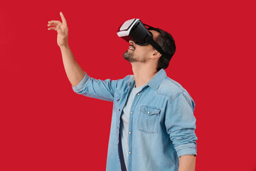 Handsome man using VR glasses on red background