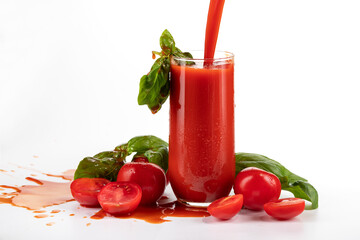 tomato juice in a glass goblet with tomatoes lying nearby on a white background
