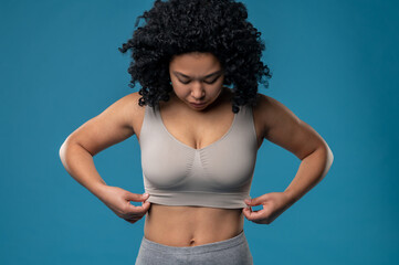 Waist up picture of woman in a bra standing on a blue background