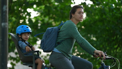 Mother and child riding bicycle kid in bike back seat wearing helmet rides together with parent