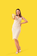 Young woman with glass of smoothie on yellow background