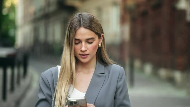 Portrait of attractive blonde woman texting message on smartphone on city street
