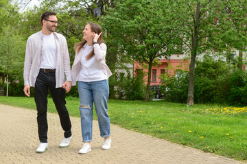 Fototapeta premium Happy young couple holding hands walking together on park path, enjoying leisure time and relationship
