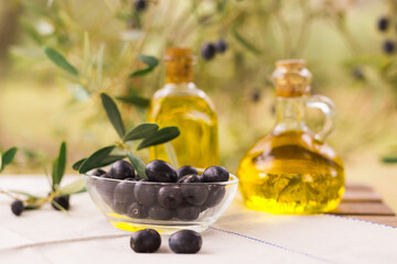 Black ripe olives, olive oil in a glass traditional bottle on table in an olive garden