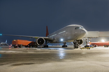 Wide body passenger airliner at the air bridge on night airport apron. Airfield tankers refuels...