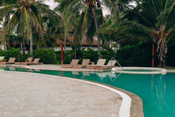 vue sur une piscine turquoise avec des chaises longue vide au bord et des palmiers en arrière