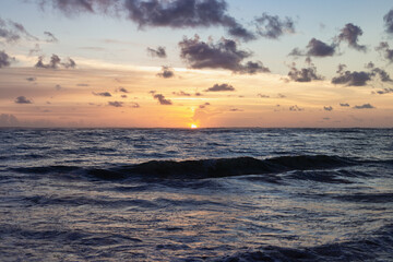 lever de soleil au dessus de l'horizon avec des petits nuages dans le ciel au dessus de l'océan avec des vagues 
