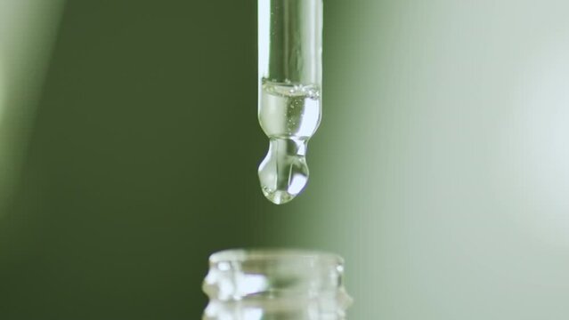 Liquid fluid oil or serum essential in pipette drips on green background. Cosmetic skin care product, beauty concept.