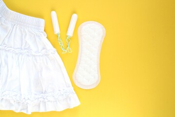 White skirt, woman sanitary pad and tampon swab on yellow background. Female menstruation cycle period. Hygiene concept. Linen and health protection idea. Copy space