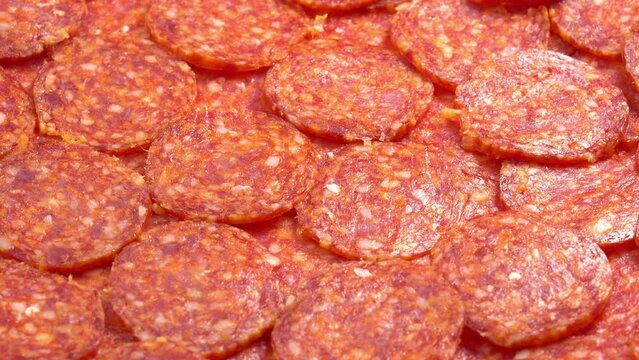 Juicy sliced pepperoni sausage rotating as background for restaurant, food video, food porn. Smoked sausage slices for pizza