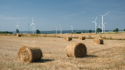 Green energy and agriculture: field with heaps of hay and wind turbines - obrazy, fototapety, plakaty