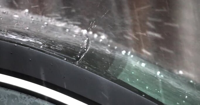 Top of a car and windshield being hit by rainy hail storm. Concept: Vehicle Hail Damage Insurance Coverage