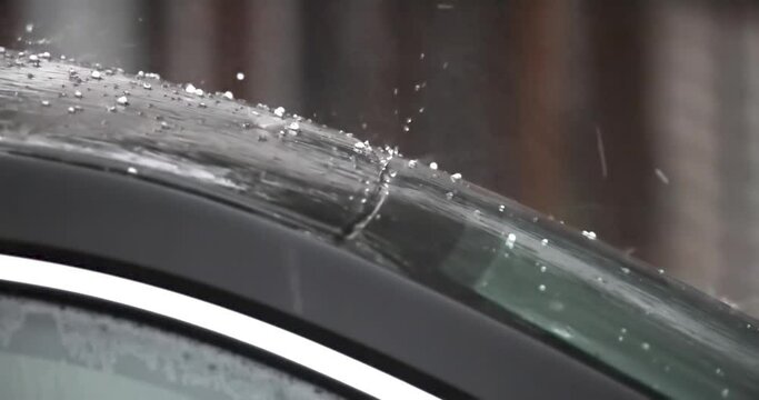 A car and windshield being hit by rainy hail storm. Concept: Vehicle Hail Damage Insurance Coverage